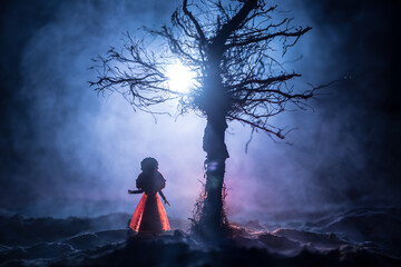Alone girl in the dead forest at misty night. Silhouette of girl standing between trees under...
