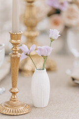 Beautiful composition made of antique bronze candlestick and white ceramic vase with three roses . 