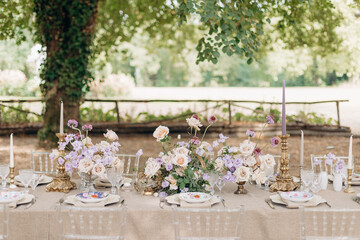 Beautiful wedding table in natural colors with bouquets of flowers and festive serving in garden. 