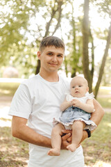 Fototapeta premium Dad's day. Smiling cute dad carefully holds his newborn daughter in his arms onsummer day outside. 