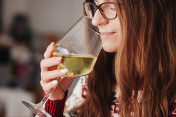 Woman drinking wine. White wine drinking. Wine glass in hand. Girl in woolen sweater alcohol. Cozy winter background. Female hand holding wine glass. Christmas pattern season clothing. Long hair.