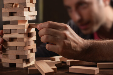 man hands making stack of wooden blocks for jenga game on dark brown table, while staying home...