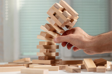 Businessman removing wooden block from falling tower on table.