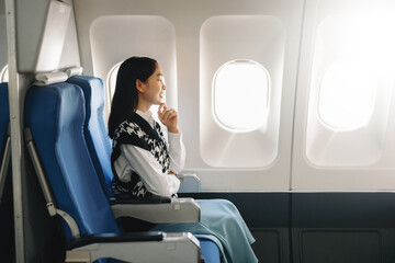 Young Asian executive excels in first class, multitasking with digital tablet, laptop and...