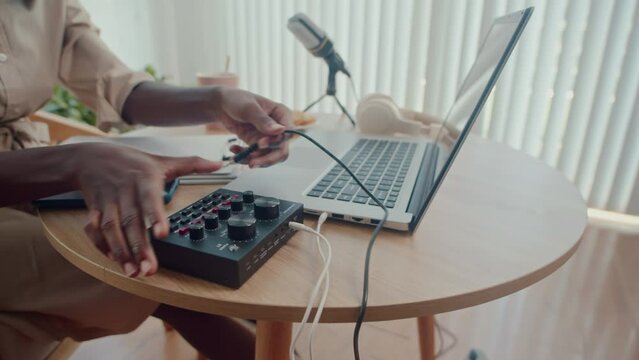 Cropped shot of female blogger connecting equipment while sitting at desk in front of laptop preparing for recording in studio