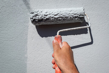 Pintor a pintar uma parede exterior com o seu rolo de pintar