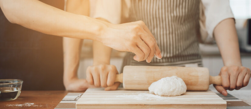 man in apron rolling out dough for homemade pastry, enjoying preparing biscuit cookies in modern light kitchen.