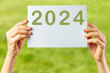 2024, Woman holding cardboard with number 2024 on green background. Happy New Year