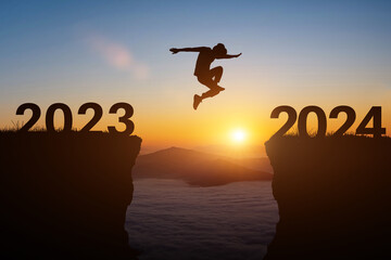 Happy new year 2024 concept. Silhouette of man jump on the cliff between 2023 to 2024 years over sunset or sunrise background. - obrazy, fototapety, plakaty