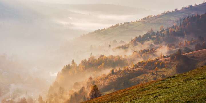 mountainous rural landscape at sunrise. forested hills in fall colors in morning light. foggy weather in autumn. view from above