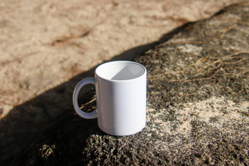 A white mug placed on a log with a view of nature in the background.