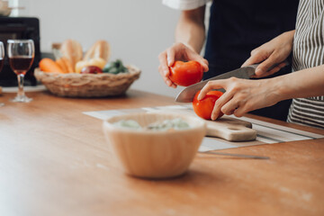 Happy asia young couple cooking together with vegetables in cozy kitchen, preparing vegetarian food colorful variety of vegetables and herbs lying on wooden kitchen table, love and valentine concept.