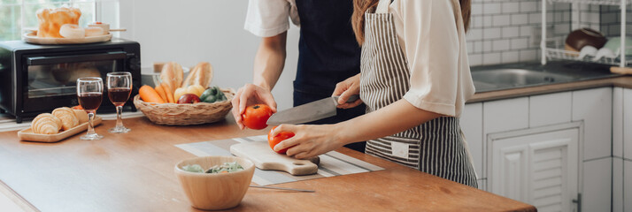 Happy asia young couple cooking together with vegetables in cozy kitchen, preparing vegetarian food colorful variety of vegetables and herbs lying on wooden kitchen table, love and valentine concept.