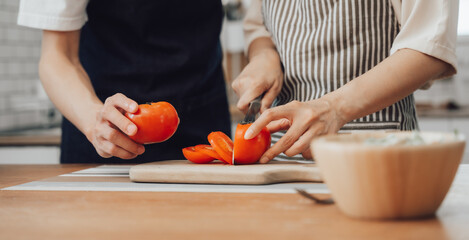 Happy asia young couple cooking together with vegetables in cozy kitchen, preparing vegetarian food colorful variety of vegetables and herbs lying on wooden kitchen table, love and valentine concept.