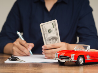 Young man in a blue shirt is filling out a car lease contract at a dealership.