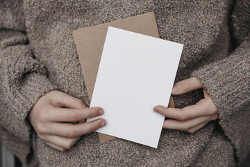 Winter, autumn cozy stationery still life. Child, female hands in beige pullower holding blank...