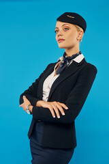 Obraz na płótnie Canvas confident woman in elegant uniform of air hostess posing with folded arms and looking away on blue