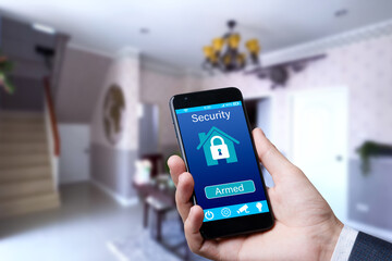 Smart home automation app on smartphone hold by male hand with home interior in background.