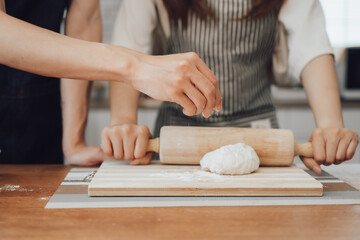 Cropped image of man wearing aprons preparing homemade pastry, kneading dough with a rolling pin on wooden table in kitchen