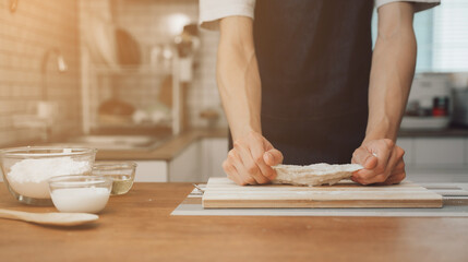 Cropped image of man wearing aprons preparing homemade pastry, kneading dough with a rolling pin on...