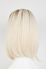 Fototapeta premium Natural looking blonde fair wig on white mannequin head. Middle length hair cut on the plastic wig holder isolated on white background, back view