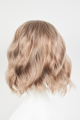 Naklejka premium Natural looking blonde fair wig on white mannequin head. Middle length hair cut on the plastic wig holder isolated on white background, back view