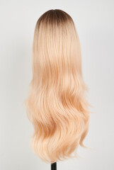 Naklejka premium Natural looking blonde wig on white mannequin head. Long hair on the plastic wig holder isolated on white background, back view.