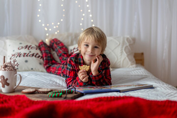 Beautiful blond child, young school boy, writing homework for school in a decorated home, drinking milk and eating cookies.