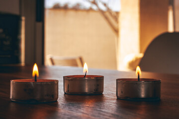 Burning candles placed against window with curtain during aromatherapy session at home