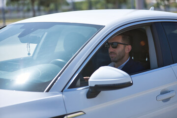 Fototapeta na wymiar Successful, attractive, young Hispanic man in jacket and sunglasses driving his white luxury car. Concept, cars, luxury, success, businessman.