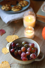 Cup of tea or coffee, plate with desserts, dried oranges, bowl of grapes, scented candles, vintage books, pumpkins and autumn leaves on the table. Autumnal hygge. Selective focus.