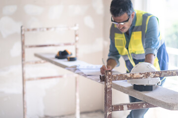 Specialist in glasses writing notes on project papers stands near construction safety equipment man in professional uniform ready for renovation process in building