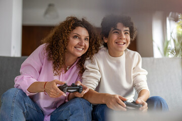 Mother and son playing video games while sitting on sofa at home
