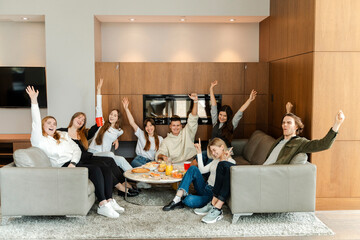 Fototapeta premium Big group of happy friends looking at camera, raising hands, having fun at home.