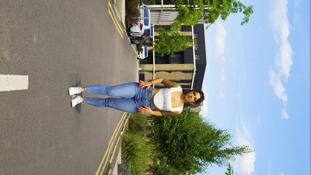 young women in her 20s tanned olive skin perfect figure standing dancing in the middle of the road modern luxurious street tight blue jeans outfit white crop shirt messy hair bun blue sky dancer model