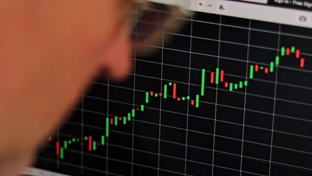 Close up slow motion footage of the mid aged man next to the computer screen with trading bar charts. Finance