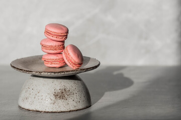 Fototapeta na wymiar Traditional French macaroons. Pink almond cookies on a stylish ceramic plate on a gray stone background. Delicious dessert.