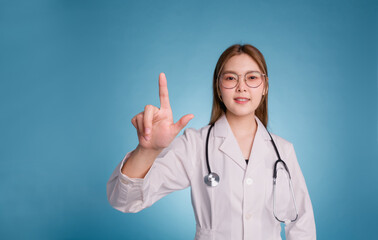 Portrait of smiling female doctor touching virtual screen. Young asian doctor wear medical uniform lab coat and stethoscope isolated over blue color background. Health science and technology concept.