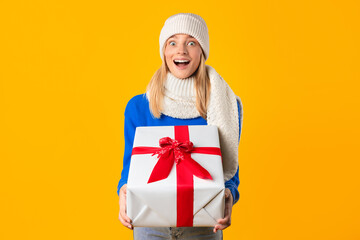 Overjoyed woman holding Christmas gift on yellow background
