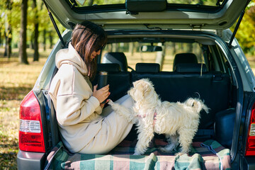 Young woman and cute dog relaxing enjoying happy moment in the forest sitting in car trunk