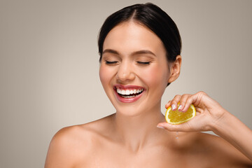 Laughing gorgeous young european lady with perfect face, hold yellow lemon fruit, has fun