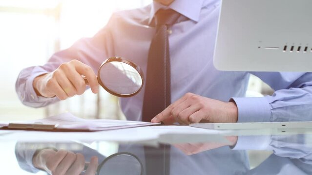 man looking through a magnifying glass to documents notebook.