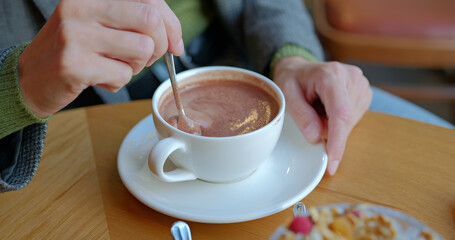 Girl hand stirs hot chocolate in white cup with spoon.