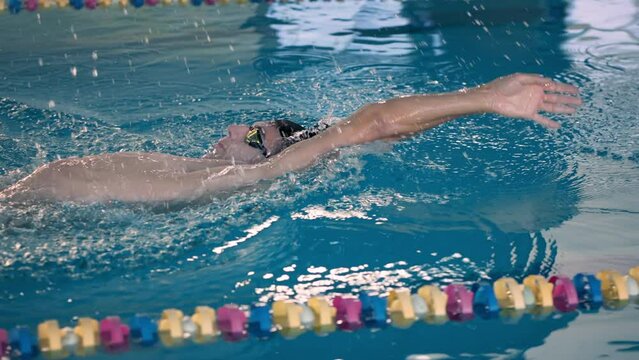 Young swimmer trains backstroke style in public pool water
