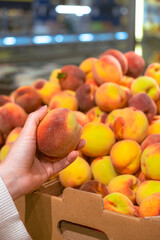 hand taking peach from grocery store shelf