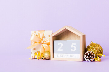 25 december. Christmas composition on colored background with a wooden calendar, with a gift box, toys, bauble copy space