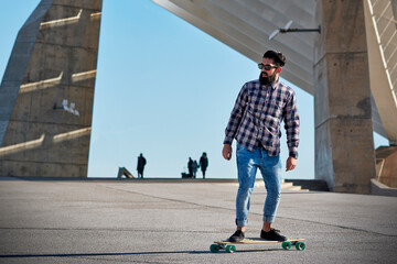 Bearded man in sunglasses riding longboard near geometric constructions