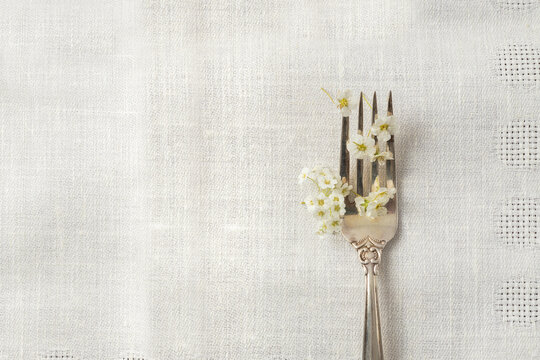 Top view of white spring flowers and elegant fork on the tablecloth.Empty space