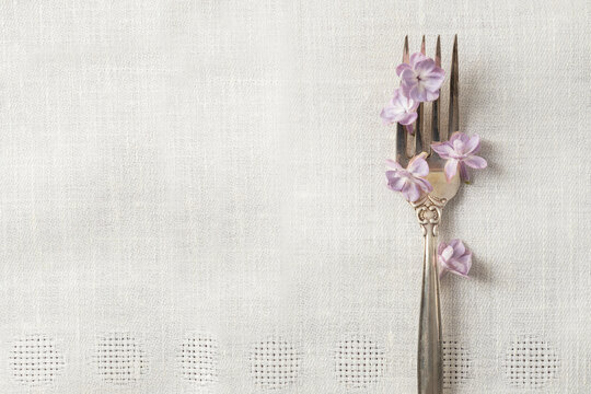 View from above of fresh lilac petals and elegant fork on the white tablecloth.Empty space