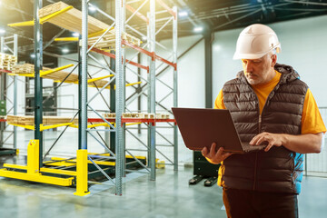 Man is storekeeper with laptop. Manager works in warehouse. Guy inside logistics center. Warehouse manager with computer. Man in hangar with warehouse racks. Contractor uses logistics software - obrazy, fototapety, plakaty